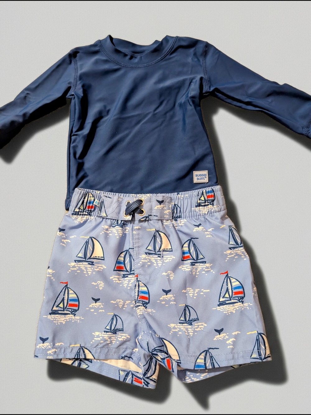 RuggedButts sailboat print two-piece rash guard swimsuit set.